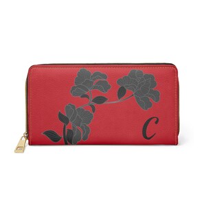 May include: Red leather zipped wallet with a black floral design and the letter "C" in black.