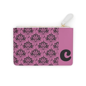 May include: A pink zipped pouch featuring a black floral design and the letter "C". The pouch has a white zip pull and a gold-coloured zip. The floral pattern is repeated across the front.