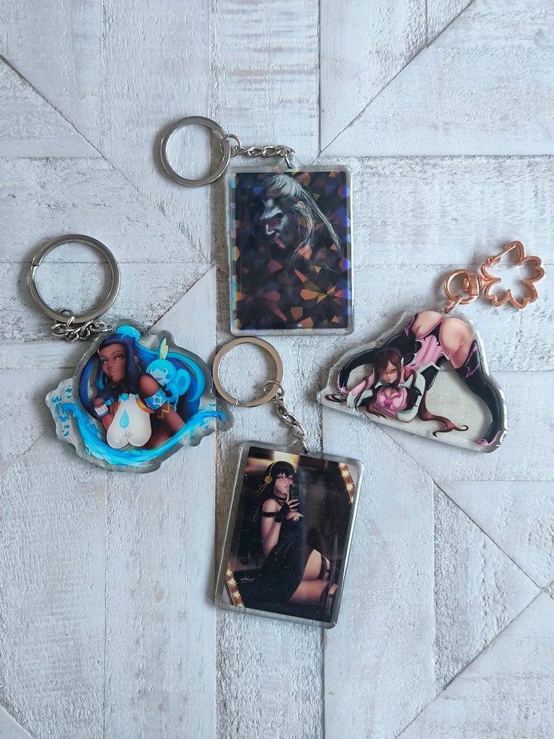 May include: Four different keychains with colorful anime-style illustrations. Each keychain features a different character with a unique design and a silver metal ring.