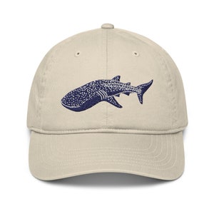 Puede incluir: Una gorra de béisbol beige con un diseño de tiburón ballena azul bordado.