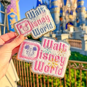Könnte beinhalten: Gestickte Aufnäher mit dem Text "Walt Disney World" in Rosa, Weiß und Grau. Die Aufnäher zeigen einen Mickey Mouse-Kopf und farbenfrohes Feuerwerk. Die Aufnäher haben einen goldglitzernden Rand.
