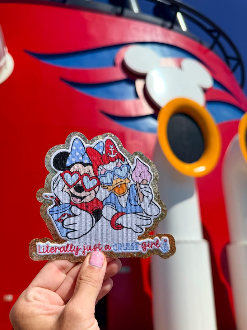 May include: A glittery embroidered patch featuring Minnie Mouse and Daisy Duck wearing heart-shaped sunglasses. Minnie holds a blue drink, while Daisy holds a pink ice cream cone. The text at the bottom reads, Literally just a CRUISE girl.
