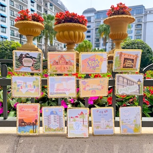 May include: A collection of twelve rectangular cards with gold glitter borders, each featuring colorful illustrations of various Disney resort hotels, including Aulani, Pop Century, Animal Kingdom Lodge, Art of Animation, and the Grand Floridian.