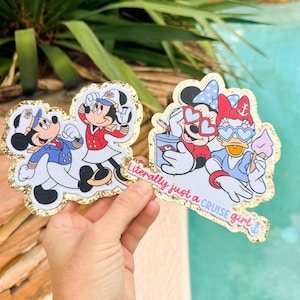 Może przedstawiać: Dwie wycinane naklejki ze złotymi brokatowymi obw&oacute;dkami. Jedna przedstawia Myszkę Miki i Minnie w mundurach rejsowych. Druga naklejka przedstawia Myszkę Minnie i Daisy w okularach w kształcie serc z napisem Literally just a CRUISE girl.