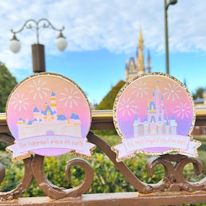 May include: Two pink and gold glitter patches with a silhouette of Cinderella's castle and fireworks. The text on the patches reads "The happiest place on earth" and "The most magical place on earth".
