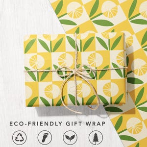 May include: A rectangular gift wrapped in paper featuring a yellow and cream checkered pattern with stylized green leaves and yellow circular floral motifs, tied with natural twine. Text reads ECO-FRIENDLY GIFT WRAP with four circular icons.