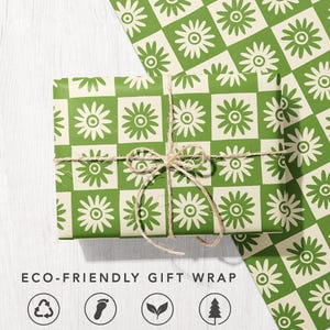 May include: A rectangular gift wrapped in paper featuring a green and cream checkered pattern with a stylised flower in each square, tied with thin brown twine. The text ECO-FRIENDLY GIFT WRAP appears below with four circular icons.