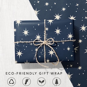 May include: A rectangular gift wrapped in dark navy blue paper featuring a pattern of cream-colored stars and dots, tied with natural jute twine. Below, the text reads ECO-FRIENDLY GIFT WRAP with four circular icons for recycled, carbon balanced, biodegradable, and sustainable paper.