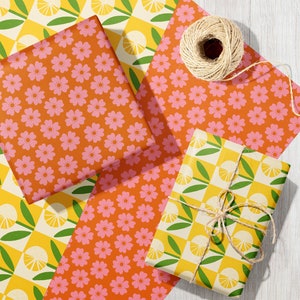 May include: Three gift boxes wrapped in different patterned paper. One box is wrapped in yellow and green checkered paper with a lemon design. Another box is wrapped in orange paper with a pink floral pattern. The third box is wrapped in orange paper with a pink floral pattern. The boxes are tied with twine.
