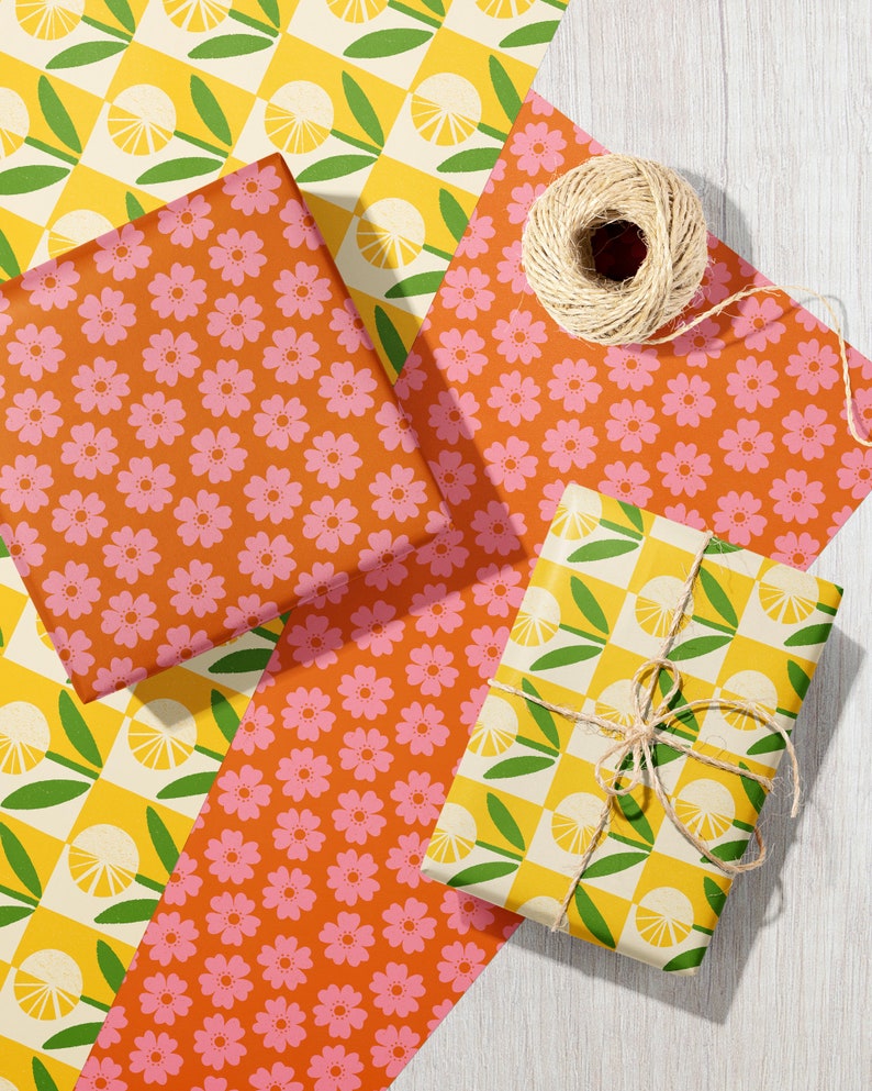 May include: Three gift boxes wrapped in different patterned paper. One box is wrapped in yellow and green checkered paper with a lemon design. Another box is wrapped in orange paper with a pink floral pattern. The third box is wrapped in orange paper with a pink floral pattern. The boxes are tied with twine.