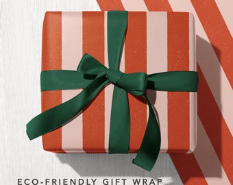 May include: A square gift box wrapped in paper with vertical stripes of terracotta orange and pale pink, tied with a dark forest green ribbon. Below the box, text reads ECO-FRIENDLY GIFT WRAP with icons for recycled, carbon balanced, and biodegradable.