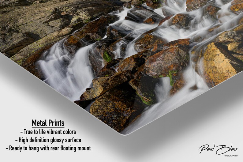 May include: Metal print featuring a cascading waterfall over rocks. The water appears white and foamy, contrasting with the brown and tan rocks. The print has a high-definition glossy surface and is ready to hang with a rear floating mount.
