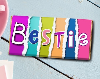 Puede incluir: Una barra de chocolate colorida con la palabra "Bestie" escrita en una fuente divertida. La barra está dividida en secciones de rosa, azul, verde, amarillo, morado, azul y rosa.