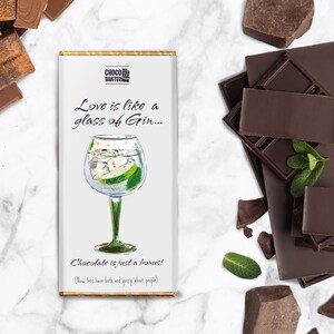 May include: A white chocolate bar with a humorous message about love and gin. The bar features a hand-drawn illustration of a gin and tonic with a lime wedge. The text reads "Love is like a glass of Gin... Chocolate is just a bonus! (Now let's have both and gossip about people)"