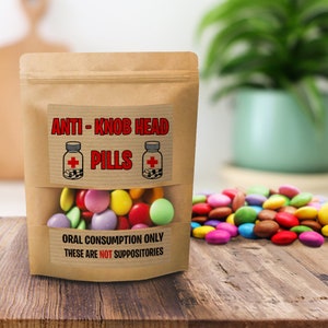 Könnte beinhalten: Ein brauner Papiertüte mit einem transparenten Fenster, gefüllt mit bunten Süßigkeiten. Auf der Tüte steht "ANTI-KNOB HEAD PILLS" und "ORAL CONSUMPTION ONLY THESE ARE NOT SUPPOSITORIES". Ein Haufen Süßigkeiten befindet sich neben der Tüte.