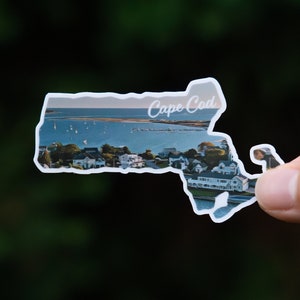 May include: A white sticker shaped like the state of Massachusetts with a photo of a coastal town and the words "Cape Cod" printed on it.