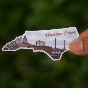 Może przedstawiać: Naklejka w kształcie Karoliny P&oacute;łnocnej, przedstawiająca panoramę Winston-Salem. Naklejka ma białą obw&oacute;dkę i napis "Winston-Salem" w ozdobnej czcionce.