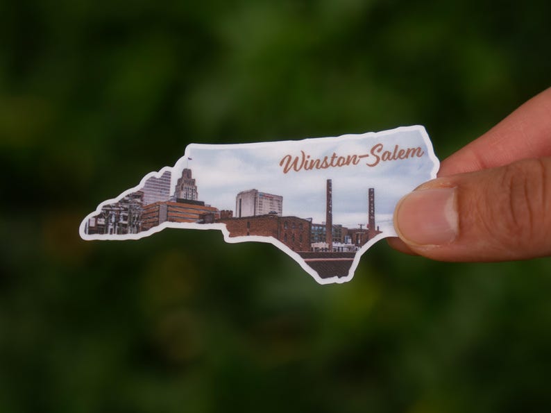 Może przedstawiać: Naklejka w kształcie Karoliny P&oacute;łnocnej, przedstawiająca panoramę Winston-Salem. Naklejka ma białą obw&oacute;dkę i napis "Winston-Salem" w ozdobnej czcionce.