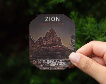 May include: A brown and white sticker with a picture of a mountain range and the text "ZION NATIONAL PARK" and "1919" with coordinates "37.2982° N, 113.0263° W".