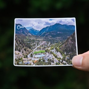 May include: A postcard with a photo of Colorado Springs, Colorado. The postcard shows a view of the city from a mountainside, with the text "Colorado Springs" printed in white at the top.