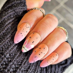 Può includere: Unghie a mandorla ombré rosa e arancio con pois neri e un design di faccia di coniglio bianco.