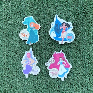 May include: Four colorful stickers featuring Disney princesses. Each sticker has a princess image and race details. One says "5K 2026", another "10K 2026", a third "HALF MARATHON 2026", and the last "FAIRY TALE CHALLENGE 2026".