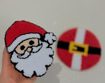 Peut inclure: Ornements de Noël faits à la main. L'un représente le visage du Père Noël avec un bonnet rouge, une barbe blanche et un contour noir. L'autre est un ornement rond représentant la ceinture du Père Noël, avec un fond rouge, une rayure blanche et une boucle jaune.
