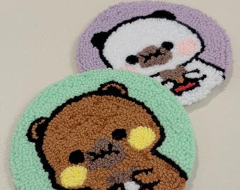 Peut inclure: Deux dessous de verre ronds faits à la main avec des motifs d'ours de dessin animé. L'un présente un ours brun sur un fond vert clair, l'autre un panda sur un fond lavande. Les deux ont des contours noirs et sont en fil texturé.