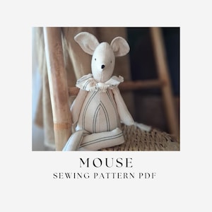 Op de afbeelding: Een knuffelmuis gemaakt van gebroken witte stof met dunne verticale donkere strepen op het lichaam en de ledematen, voorzien van een ruchekraag en een kleine zwart gestikte neus. De tekst MOUSE SEWING PATTERN PDF staat onder het speelgoed.