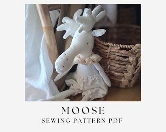 May include: A white fabric moose doll with large antlers, a ruffled beige collar, and cream-colored bloomers. The text below the doll reads MOOSE SEWING PATTERN PDF. The doll features simple stitched facial details and a soft, stuffed construction.
