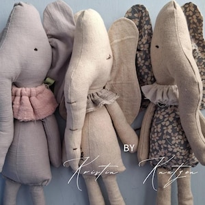 May include: Three stuffed elephant toys in light gray, beige, and patterned fabric. Each elephant features a ruffled collar, long trunks, and large ears. The right elephant has a floral pattern on its body and ears. Text reads BY Kristin Knutzen.