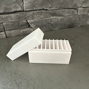 Può includere: Scatola di contenimento in plastica bianca con coperchio e più scomparti. La scatola è aperta e il coperchio è appoggiato sopra.