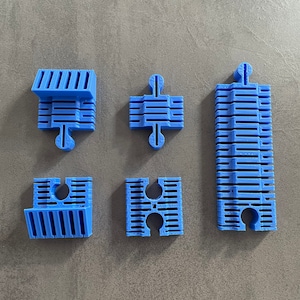 Può includere: Sei pezzi di puzzle in plastica blu con un motivo a griglia. I pezzi sono disposti in due file di tre.
