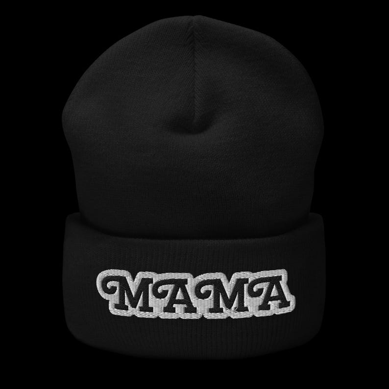 May include: A black beanie hat with the word "MAMA" embroidered in white across the front. The hat is made of a soft, knitted material. This warm hat is a stylish accessory for the head.