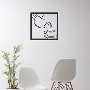 Peut inclure: Une œuvre d'art murale en métal noir représentant une théière versant du thé dans une tasse. L'œuvre est encadrée dans un carré noir et est accrochée à un mur blanc. Deux chaises blanches avec des pieds en bois sont au premier plan.