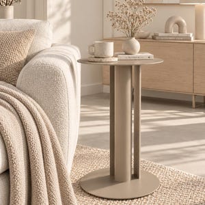 May include: A beige side table with a circular top and a central cylindrical base supported by three vertical panels. The table is constructed from a smooth, matte-finished material and features a clean, structural design that stands on a flat base.