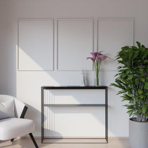 Può includere: Scena d'interni moderna con una parete bianca con tre opere d'arte incorniciate. Un tavolino nero ospita un vaso di fiori viola e una statua decorativa. Una poltrona bianca e una pianta in vaso completano l'arredamento.