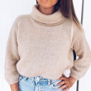 May include: A beige turtleneck sweater with a loose fit and long sleeves. The sweater is made of a soft, knitted fabric.
