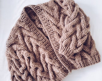 May include: A chunky knit cardigan in a light brown colour with a cable knit pattern. The cardigan is open at the front and has long sleeves.
