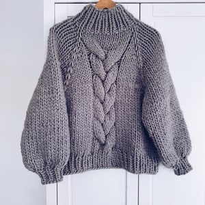 May include: A gray chunky knit sweater with a cable knit design and a high neck.