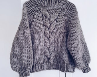 May include: A gray chunky knit sweater with a cable knit design and a high neck.