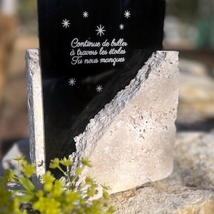May include: A memorial stone with a black, rectangular top featuring white star designs and the French text "Continue de briller à travers les étoiles Tu nous manques." The base is a light-coloured, textured stone.