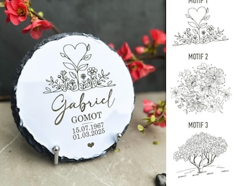 May include: A white slate plaque with a black border, featuring a heart-shaped tree with flowers and leaves. The text "Gabriel Gomot 15.07.1967 01.03.2025" is engraved below the tree.