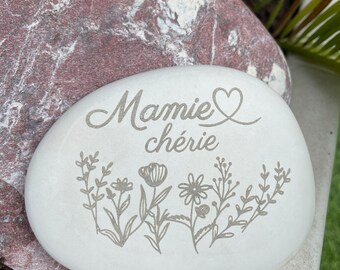 Può includere: Pietra bianca con le parole "Mamie chérie" incise, con un simbolo di cuore accanto al nome. La pietra è decorata con una fila di piccoli fiori incisi.
