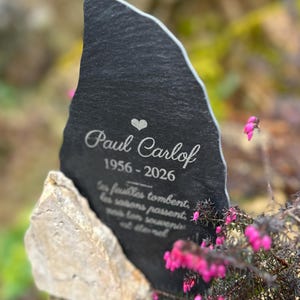 Peut inclure: Une plaque commémorative en ardoise gris foncé aux bords irréguliers, gravée d'un cœur, du nom Paul Carlof, des dates 1956-2026 et du texte : Les feuilles tombent, les saisons passent, mais ton souvenir est éternel, soutenue par une pierre claire.