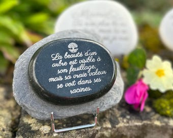 May include: A black stone with a silver stand, featuring an engraved quote in French: "La beauté d'un arbre est visible à son feuillage, mais sa vraie valeur se voit dans ses racines."
