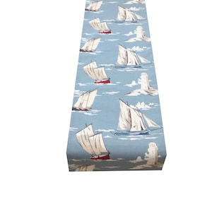 Könnte beinhalten: Ein blauer Tischläufer mit einem sich wiederholenden Muster aus weißen Segelbooten und roten Booten auf blauem Hintergrund. Die Boote segeln auf einem blauen Meer mit weißen Wolken und einem weißen Leuchtturm.