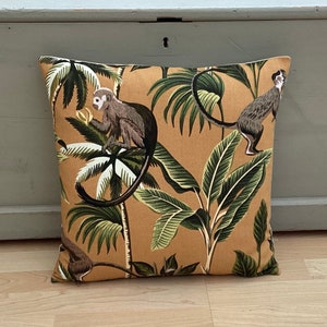 May include: A tan throw pillow with a tropical print featuring monkeys and palm trees. The pillow has a brown border.