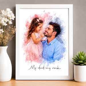 Peut inclure: Impression artistique encadrée avec un père et sa fille. La fille, vêtue d'une robe rose, semble appliquer du rouge à lèvres à son père. Le fond présente des éclaboussures d'aquarelle roses et bleues. Le texte "My dad my rock" est en bas.