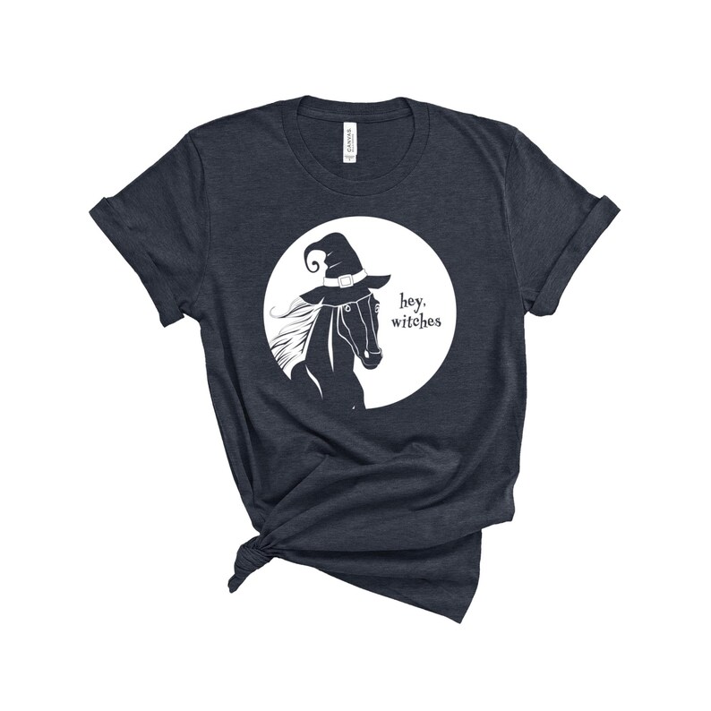 May include: A dark blue t-shirt with a white graphic of a horse wearing a witch's hat. The text "hey, witches" is printed below the horse.